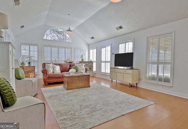 living area with light wood finished floors, plenty of natural light, visible vents, and vaulted ceiling