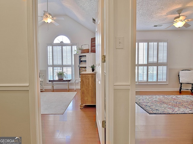 interior space with light wood-style flooring, visible vents, vaulted ceiling, and a textured ceiling