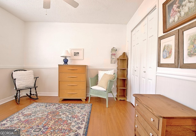 living area featuring light wood-style floors, a ceiling fan, a textured ceiling, and wainscoting