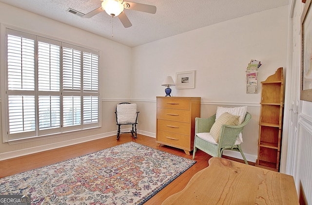 living area featuring a textured ceiling, wood finished floors, visible vents, and a ceiling fan