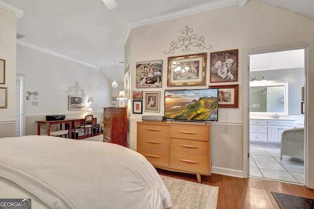 bedroom featuring vaulted ceiling, crown molding, light wood-style flooring, and ensuite bath