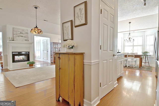 corridor with a textured ceiling, a chandelier, lofted ceiling, baseboards, and light wood finished floors