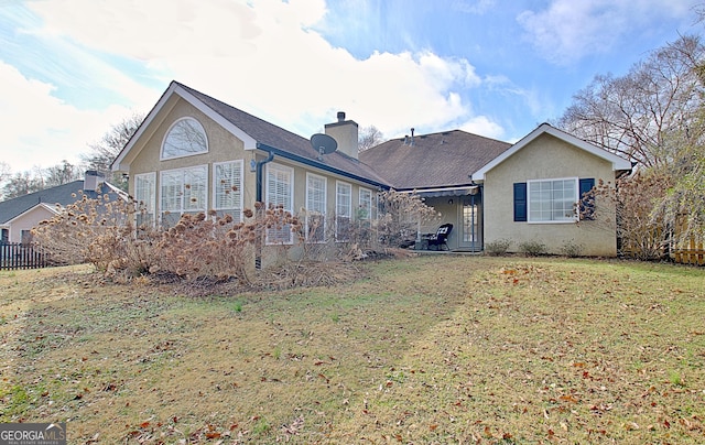 rear view of property featuring a yard, a chimney, and stucco siding