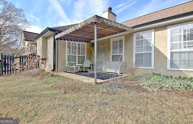 back of property with a yard, a chimney, stucco siding, a patio area, and fence