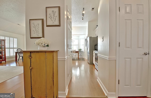 corridor with a healthy amount of sunlight, light wood finished floors, visible vents, and a textured ceiling