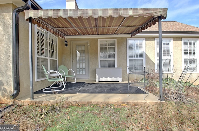 view of exterior entry featuring a shingled roof, a patio, and stucco siding