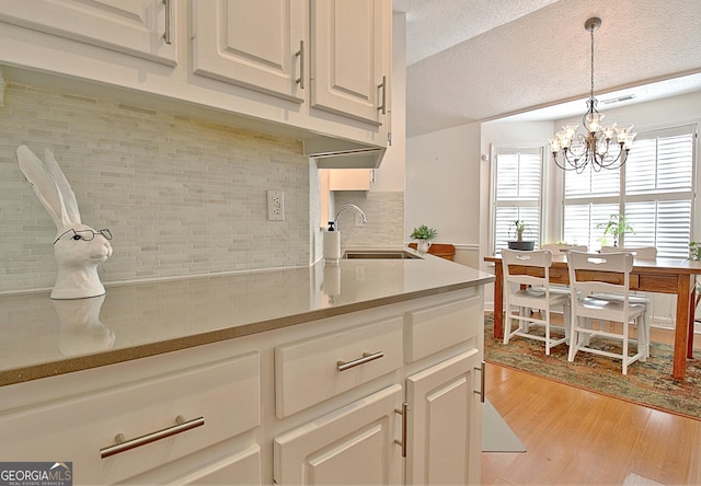 kitchen with decorative light fixtures, light countertops, white cabinets, a sink, and light wood-type flooring