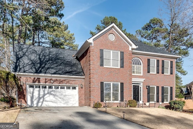 colonial home with a garage, aphalt driveway, roof with shingles, and brick siding