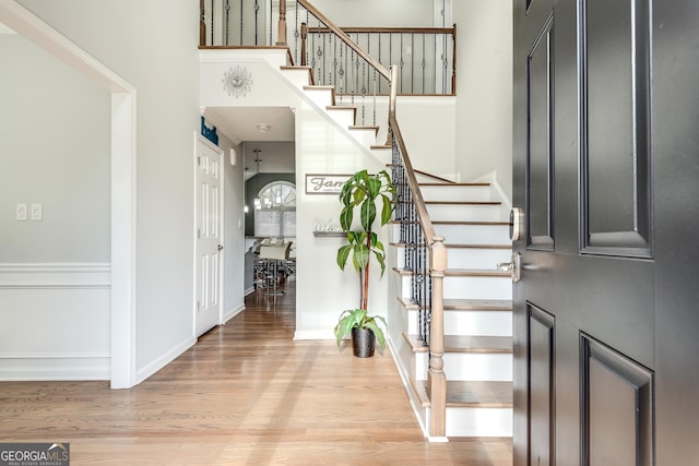 foyer with stairway, a towering ceiling, light wood-style flooring, and baseboards