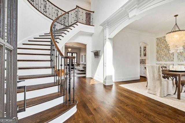 entrance foyer featuring arched walkways, crown molding, a towering ceiling, dark wood-type flooring, and a chandelier