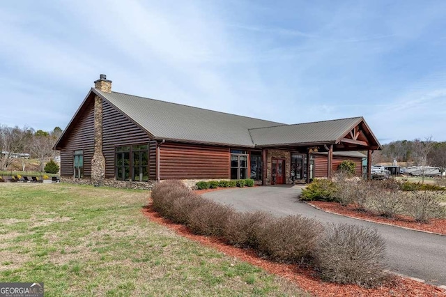 view of front of home featuring metal roof, a chimney, a front yard, and driveway