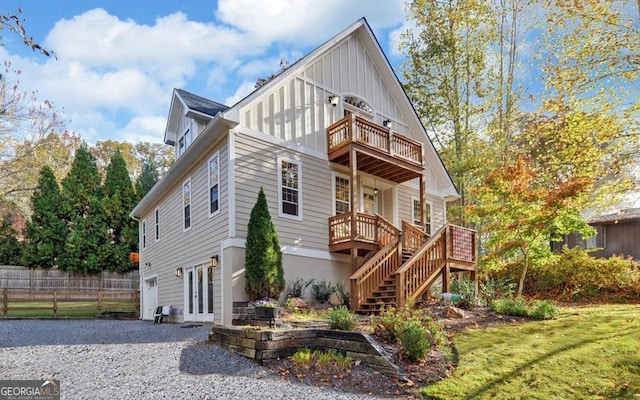 view of front of property featuring board and batten siding, a front yard, fence, a balcony, and stairs