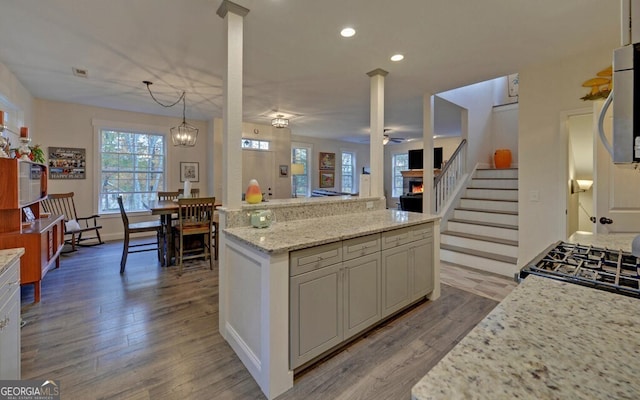 kitchen featuring light wood finished floors, range, light stone counters, stainless steel microwave, and decorative light fixtures