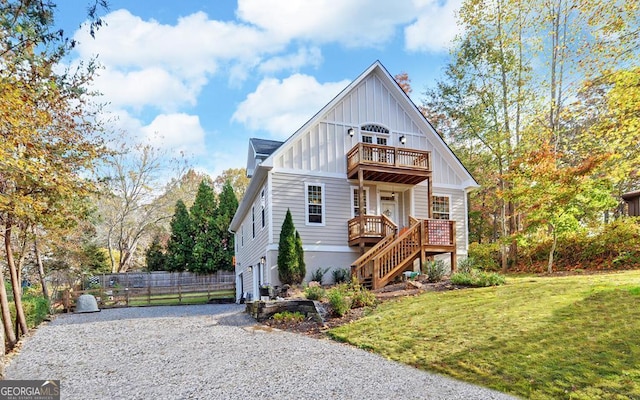 view of front of home featuring stairway, board and batten siding, fence, a balcony, and a front lawn