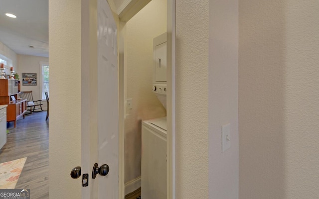 washroom with a textured wall, wood finished floors, and stacked washer / drying machine