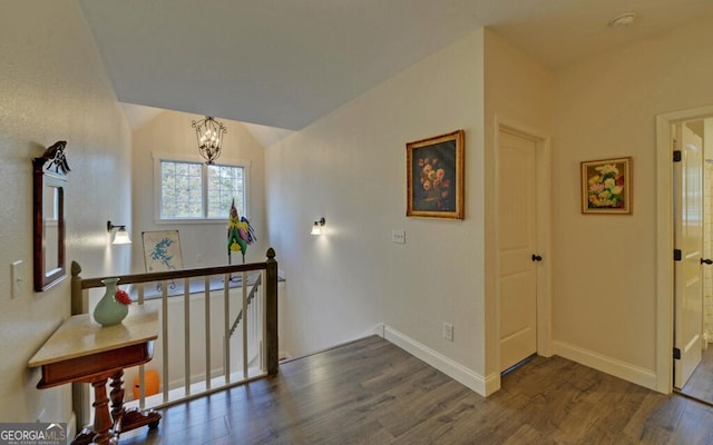 hall with lofted ceiling, a chandelier, dark wood-type flooring, an upstairs landing, and baseboards