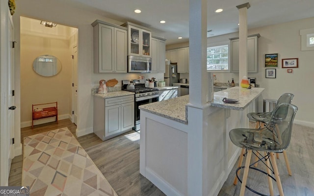 kitchen with light stone counters, stainless steel appliances, a peninsula, a kitchen bar, and glass insert cabinets