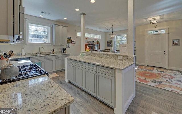 kitchen with light stone counters, visible vents, hanging light fixtures, a sink, and a kitchen island