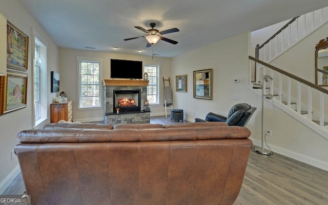 living area featuring a stone fireplace, stairway, wood finished floors, and baseboards