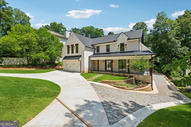 modern inspired farmhouse featuring metal roof, an attached garage, a standing seam roof, decorative driveway, and a front lawn