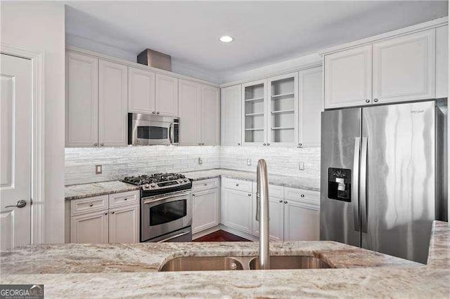 kitchen featuring stainless steel appliances, a sink, white cabinets, light stone countertops, and glass insert cabinets