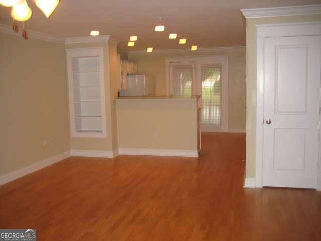 unfurnished living room with baseboards, a notable chandelier, wood finished floors, and crown molding