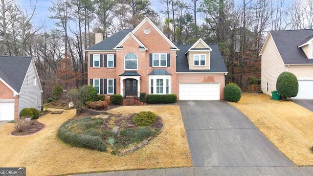 colonial-style house featuring a garage, driveway, brick siding, and a chimney