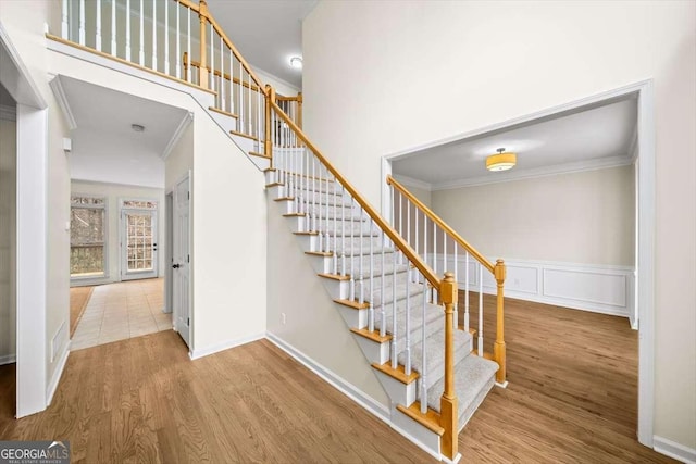 stairway featuring a wainscoted wall, ornamental molding, wood finished floors, and a decorative wall