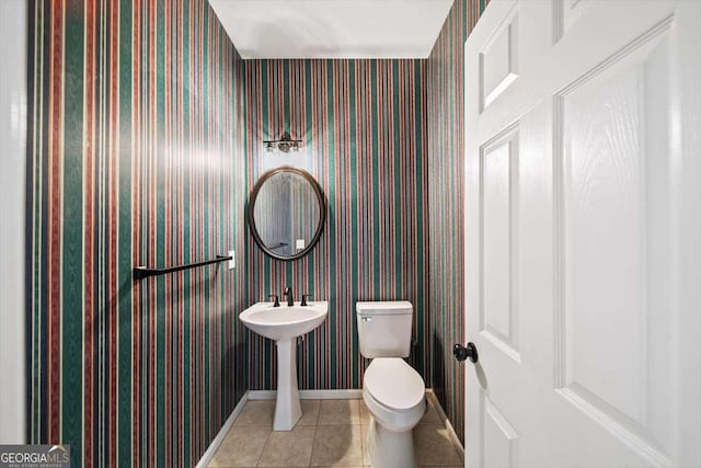 half bathroom with baseboards, tile patterned floors, toilet, and wallpapered walls