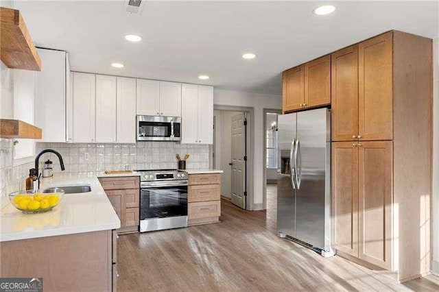 kitchen with a sink, white cabinets, light countertops, appliances with stainless steel finishes, and light wood-type flooring