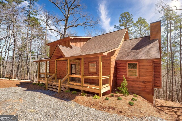 view of front of house featuring a porch, a chimney, and a shingled roof