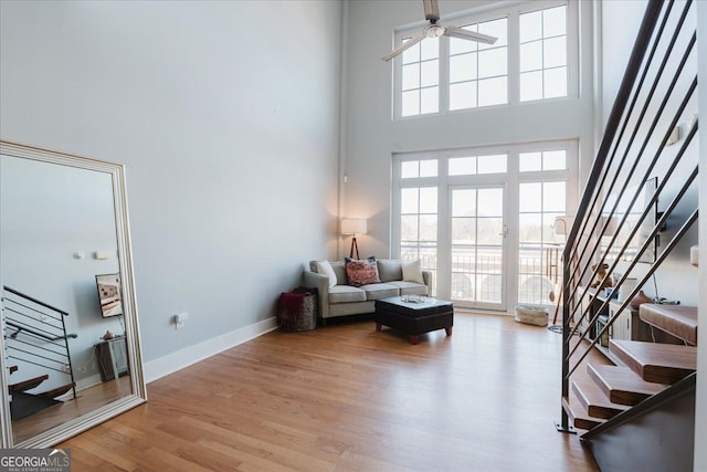 living area with a towering ceiling, a ceiling fan, wood finished floors, baseboards, and stairs