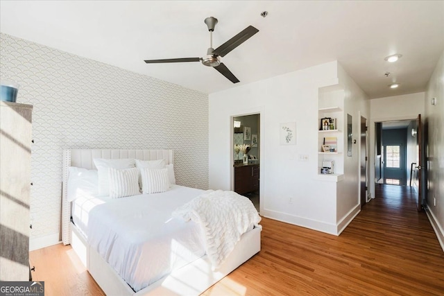 bedroom featuring baseboards, an accent wall, wood finished floors, and wallpapered walls