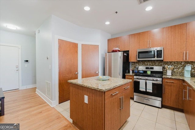kitchen with stainless steel appliances, visible vents, brown cabinets, and a kitchen island