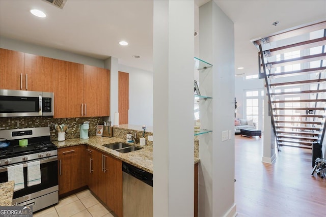 kitchen with brown cabinets, appliances with stainless steel finishes, a sink, and light stone counters