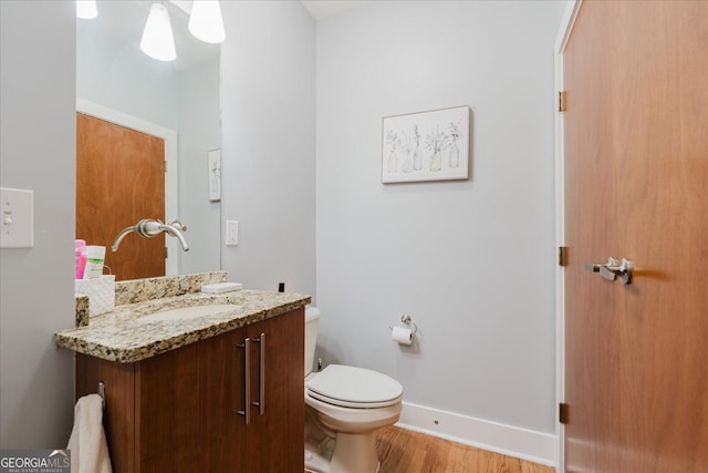 half bath featuring toilet, baseboards, wood finished floors, and vanity