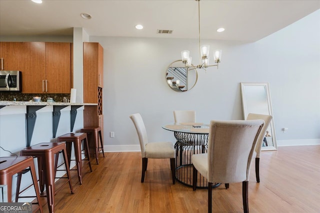 dining room featuring baseboards, light wood finished floors, a notable chandelier, and visible vents