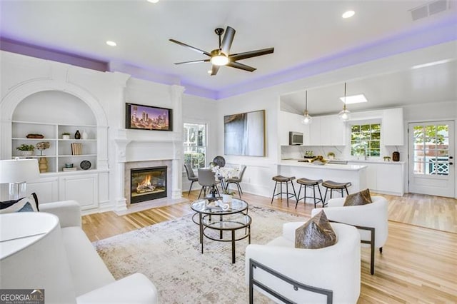 living area featuring built in shelves, a fireplace, recessed lighting, visible vents, and light wood-type flooring