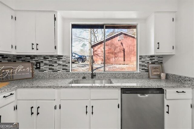 kitchen with tasteful backsplash, stainless steel dishwasher, a sink, and white cabinets