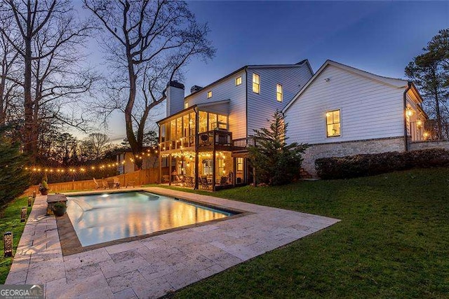 pool at dusk with a patio, a yard, fence, and a fenced in pool