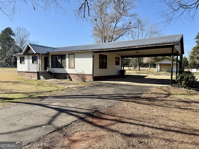 view of front facade with metal roof, driveway, a carport, and an outbuilding