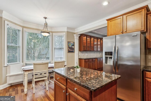 kitchen with a center island, pendant lighting, stainless steel refrigerator with ice dispenser, glass insert cabinets, and ornamental molding