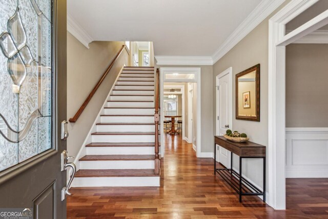 foyer entrance with dark wood-style floors, stairway, a decorative wall, and crown molding