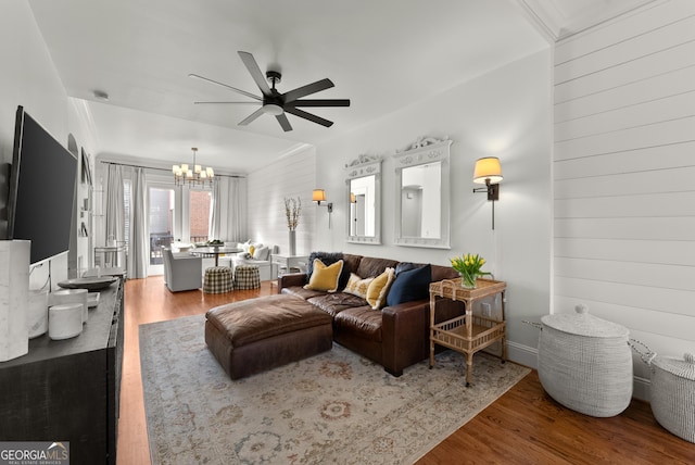 living area featuring ceiling fan with notable chandelier, wooden walls, and wood finished floors