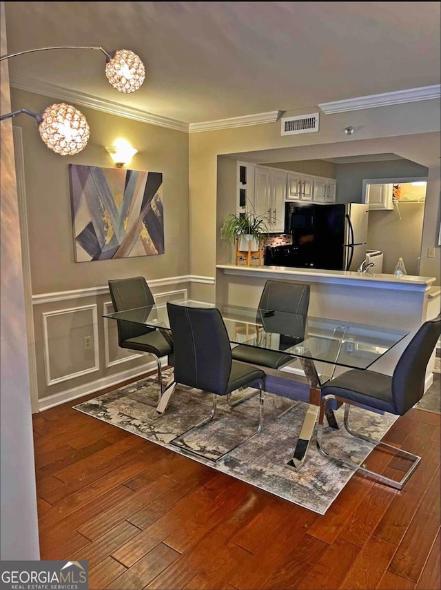 dining area with a wainscoted wall, visible vents, a decorative wall, ornamental molding, and wood finished floors