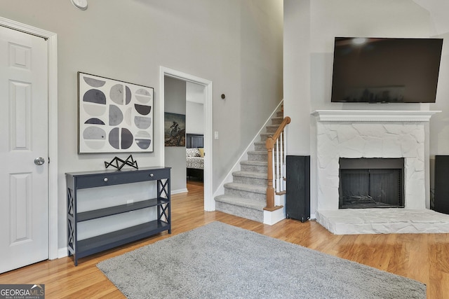 living area featuring baseboards, stairway, a fireplace with raised hearth, and wood finished floors