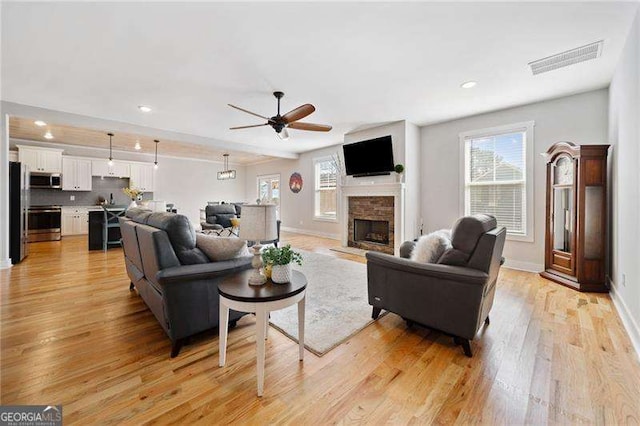 living area with a fireplace with raised hearth, light wood finished floors, plenty of natural light, and visible vents