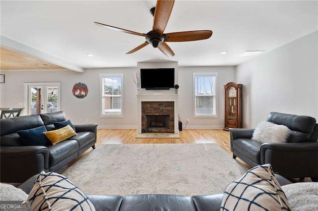 living area featuring baseboards, ceiling fan, wood finished floors, a stone fireplace, and french doors