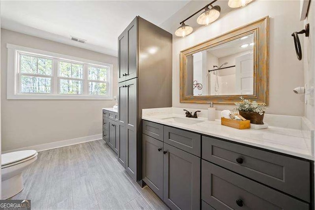 bathroom featuring toilet, vanity, visible vents, baseboards, and walk in shower