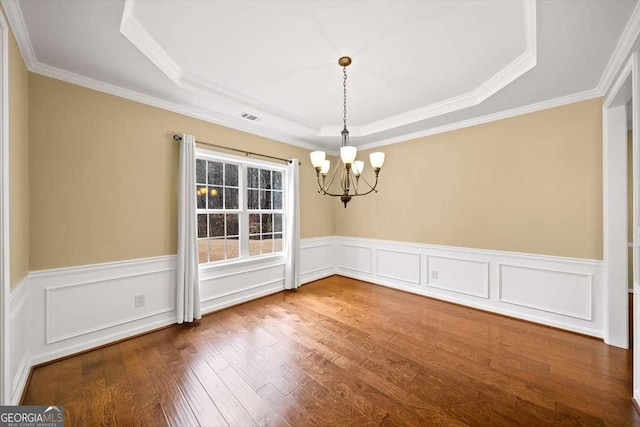 unfurnished dining area with a raised ceiling, visible vents, an inviting chandelier, wainscoting, and wood finished floors